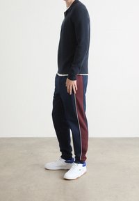 Marinblå pikétröja med lång ärm och marinblå mjukisbyxor med vinröda sidoränder och vit kantning, kombinerade med vita sneakers med blå detaljer.