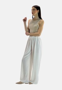 Beige ærmeløs top kombineret med løstsiddende hvide bukser, der har elastisk talje og letbrusende stof. Enkel, minimalistisk design.