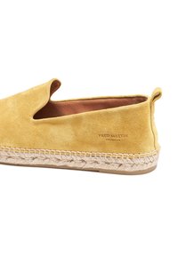Zapato amarillo de ante tipo slip-on con suela de yute trenzado, que presenta un diseño troquelado y una marca en relieve en el lateral.