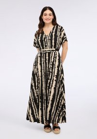 Vestido maxi con un patrón de tie-dye en franjas negras y beige, con escote en V, mangas cortas y bolsillos laterales. Se llevan sandalias de plataforma de esparto.