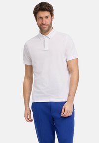 Witte polo met korte mouwen, een kraag en een voorste sluiting, gecombineerd met blauwe broek. De stof lijkt glad met een getailleerd ontwerp.