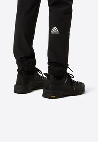 Čierne turistické topánky majú textúrovaný zvršok, spevnenú pätu a podrážku Vibram. Reflexné prvky zvyšujú viditeľnosť.