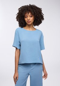 Top di un blu chiaro testurizzato con maniche corte, scollo rotondo e vestibilità rilassata, abbinato a pantaloni coordinati. Tessuto morbido e liscio.