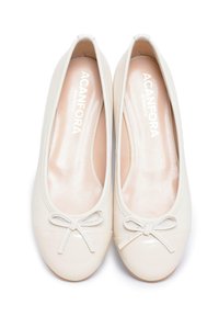 Ballerine color crema con punta in vernice, tomaia in pelle liscia e un fiocco decorativo sul davanti. Fodera interna morbida visibile.