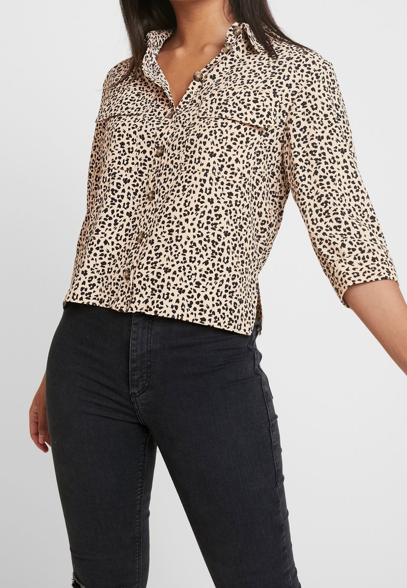 Animal print blouse in beige and black, featuring a button-up front, collar, and two chest pockets; fabric appears smooth and lightweight.