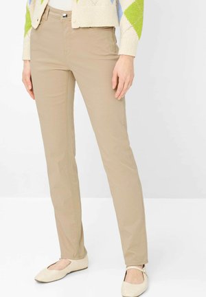 Beige slim-fit pants worn with a cream sweater featuring green and blue diamond patterns, paired with cream flat shoes with ankle straps.