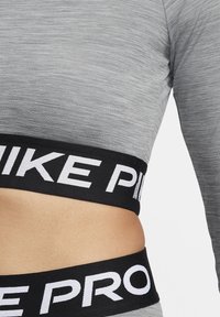 Top corto atlético gris con un diseño texturizado y una banda elástica negra que presenta la marca blanca Nike Pro.