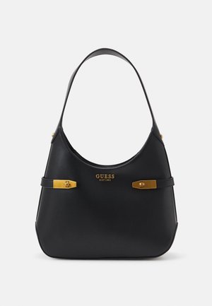 Sac à main Guess noir avec une seule bandoulière, boucles ton or sur les côtés, et texte logo doré "GUESS EST 1981" au centre avant.