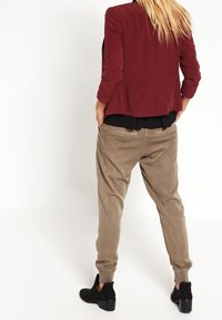 Blazer bordeaux à coupe ajustée, associé à un pantalon ample couleur beige. Les deux pièces sont en tissu doux. Des bottines noires complètent la tenue.