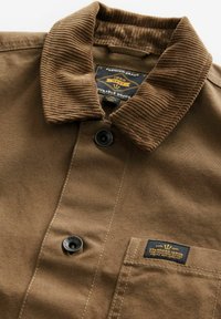 Brown canvas shirt with a ribbed collar, two buttons, and an attached label. Textured fabric with visible stitching details.