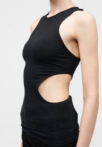 Λεπτό άτομο που φοράει μαύρο τοπ χωρίς μανίκια με μεγάλο κυκλικό άνοιγμα στο πλάι, εμφανίζοντας το δέρμα από τα πλευρά μέχρι τη μέση.