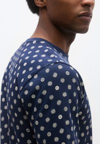 Μακρυμάνικο πουκάμισο σε ναυτικό μπλε, κατασκευασμένο  από μαλακό ύφασμα, με ολοκληρωμένο σχέδιο από μοτίβα ήλιου και φεγγαριού σε ανοιχτό κρεμ χρώμα. Κοντινή όψη του ώμου.