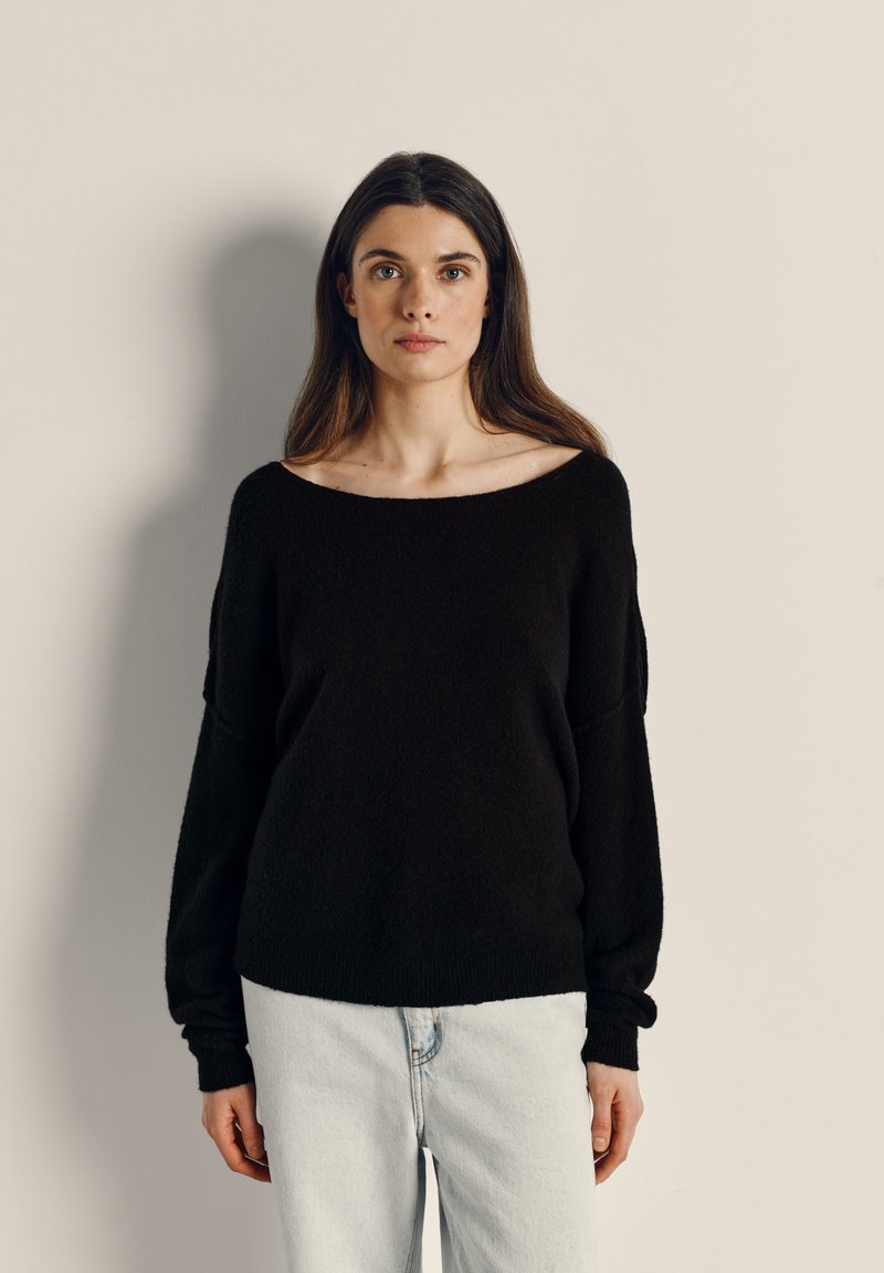 Svart, oversized tröja med bred halsringning, långa ärmar och mjuk textur, kombinerad med ljusblå jeans. Minimalistisk design.