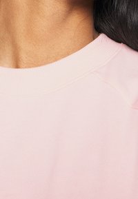 Felpa rosa chiaro con scollo a costine e texture morbida, con cuciture visibili e una vestibilità rilassata nella zona del collo.