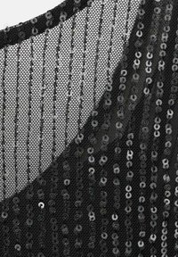 Svart meshtyg med vertikala rader av små glänsande svarta paljetter, som skapar ett randigt, strukturerat mönster.