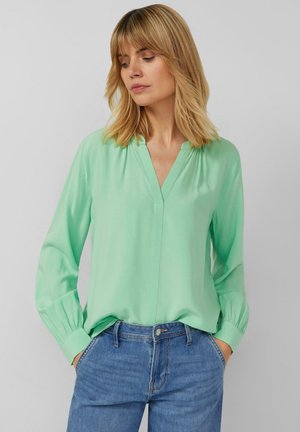 Mintgroene blouse van lichtgewicht stof, met een V-hals, lange mouwen met geplooide manchet, en een losse pasvorm. Casual denim broek.