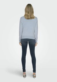 Hellblaues Sweatshirt mit langen Ärmeln und rundem Halsausschnitt, kombiniert mit dunklen Skinny-Jeans und silbernen High-Heelsandalen.