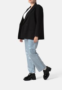 Blazer nero oversize, top bianco, pantaloni ampi azzurro chiaro e scarpe con plateau nere lucide con suola testurizzata e dettagli in pizzo.