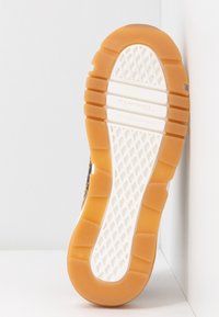 Semelle de chaussure avec une surface extérieure en caoutchouc beige, présentant un motif en grille blanche et des rainures texturées pour l'adhérence et la flexibilité.