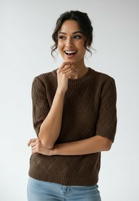 Brązowy sweter na drutach z teksturowanym wzorem warkoczowym, krótkimi rękawami i okrągłym dekoltem, zestawiony z jasnoniebieskimi jeansami.