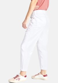 Witte high-waisted jeans met een relaxed fit, voorzien van vijf zakken en subtiele stiksels, gecombineerd met roze en rode casual sneakers.