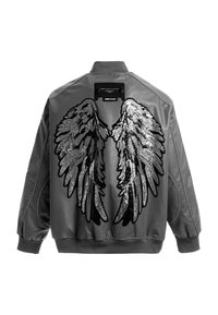 Chaqueta bomber gris con un diseño de alas de lentejuelas negras brillantes en la parte posterior. Presenta puños y cuello acanalados. Textura suave similar al cuero.