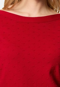 Pull rouge en tricot avec un large col bateau et une texture en points saillants sur tout le tissu pour un intérêt visuel accru.