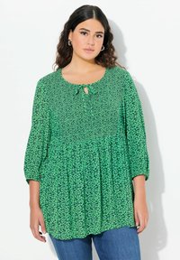 Blusa floreale verde con scollo rotondo, dettaglio a chiave e maniche a tre quarti. Tessuto leggero con un motivo testurizzato.