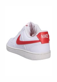 Sneaker blanche avec un extérieur en cuir lisse, des accents rouges et le logo Nike sur le talon. Dotée d'une semelle en caoutchouc texturée et d'un col rembourré.
