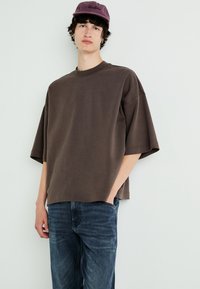 Barna, oversized pamut pulóver, rövid ujjakkal, széles nyakkal és laza fazonnal, sötét farmernadrággal párosítva.