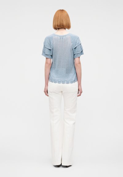 Haut tricoté bleu clair à côtes avec manches courtes volantées et ourlet festonné. Associé à un pantalon blanc à jambes droites. Design minimaliste.