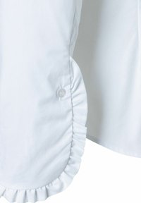 Weiße Hemd-Details mit einer Rüsche am Ärmel und einem klaren Knopf. Glattes Gewebe mit einer weichen Textur.