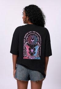 Svart oversized t-skjorte med et fargerikt sommerfugl- og solgrafikk på baksiden, med hvit tekst og et avslappet passformdesign.