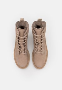 Bottines en cuir tan avec bouts ronds, design à lacets, détails cousus, pattes latérales et surface texturée. La semelle semble durable et offrant un bon soutien.