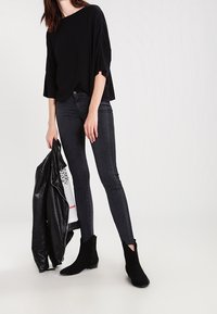 Černý over-sized top, tmavé úzké džíny, černé kotníkové boty a černá kožená bunda. Jednoduchý design s volným střihem a hladkou texturou.