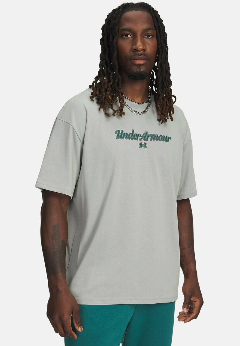 Hele hall puuvillane lühikeste varrukatega T-särk, millel on roheline "Under Armour" logo, kantud koos sinaka tooniga pükstega.