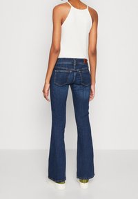 Ciemnoniebieskie dżinsy w fasonie dzwonów wykonane z denimu, z średnim stanem. Posiadają dwie tylne kieszenie oraz brązowy skórzany akcent na pasku.