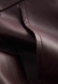 Bordeaux leren stof met een gladde textuur en zichtbare stikseldetails, waarop een gevouwen sectie is te zien voor diepte en dimensie.