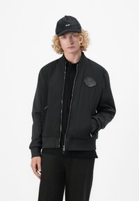 Black bomber jacket with contrasting gray sleeves, ribbed cuffs, and waistband. Features a front zipper and an embroidered logo patch.