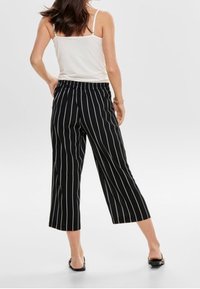 Pantalon court rayé noir et blanc en tissu léger avec une ceinture élastique, associé à un débardeur blanc simple.