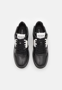 Sneakers in pelle nera con motivo perforato, dettagli bianchi, lacci neri e linguette marchiate con "GUESS EST. 1981."