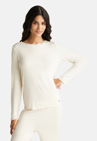 Dlouhý rukáv krémový top s texturovaným žebrovaným vzorem a krajkovým lemem kolem výstřihu; měkká tkanina s volným střihem.