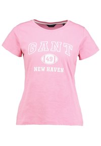 Růžové tričko s krátkým rukávem a bílým nápisem "GANT," fotbalová grafika s "49," a "NEW HAVEN" tištěné na přední straně.