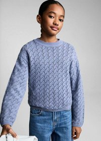 Hellblau gestrickter Pullover mit gewelltem Muster, Rundhalsausschnitt und überschnittenen Schultern, kombiniert mit hellblauen Jeans.