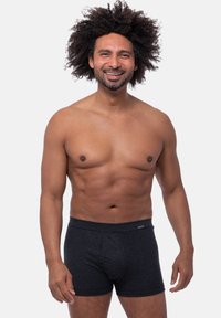 Boxer briefs a righe nere con una morbida cintura elastica, progettati in uno stile aderente, esposti su un modello maschile a torso nudo contro uno sfondo bianco.