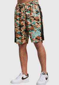 Kamuflasjonsshorts i brun, grønn og blå med elastisk midje og svarte sidelapper, med en hvit logo i en leken skrifttype.