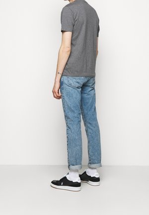 Camiseta de algodón gris, jeans de denim azul claro, zapatillas negras con suelas blancas y calcetines blancos hasta el tobillo; enfocándose en un atuendo casual desde atrás.