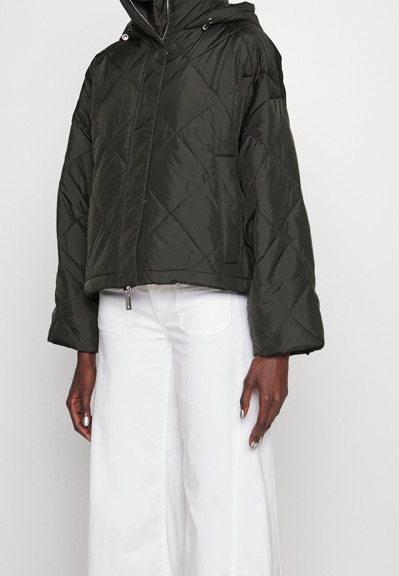Giacca a vento trapuntata di colore verde scuro con cappuccio e maniche lunghe. Presenta tasche laterali, una chiusura con zip e un orlo corto.