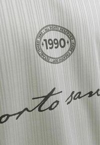 Logo circulaire avec "1990" au centre, entouré du texte "Tous droits réservés, Core Creative Dept, Établi en 1990" sur un tissu rayé gris et blanc.