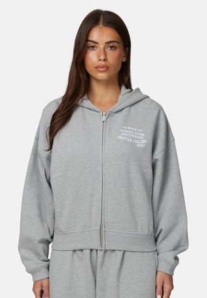 Szara bluza z kapturem na zamek, wykonana z miękkiego materiału, o luźnym kroju, z kieszeniami kangurzymi i białym napisem na piersi.